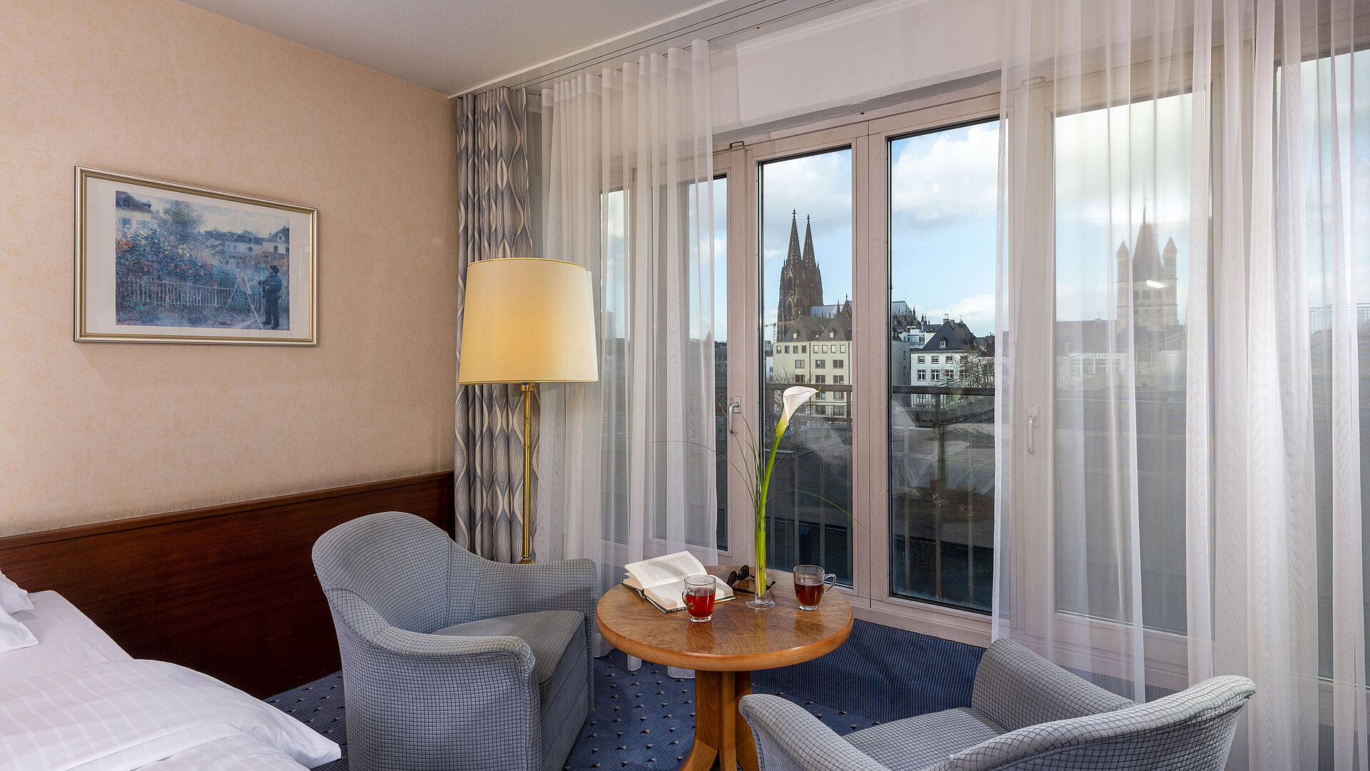 Standard-Twin Zimmer im Maritim Hotel Köln mit zwei Sesseln und Tisch, großem Fenster und Blick auf den Kölner Dom.