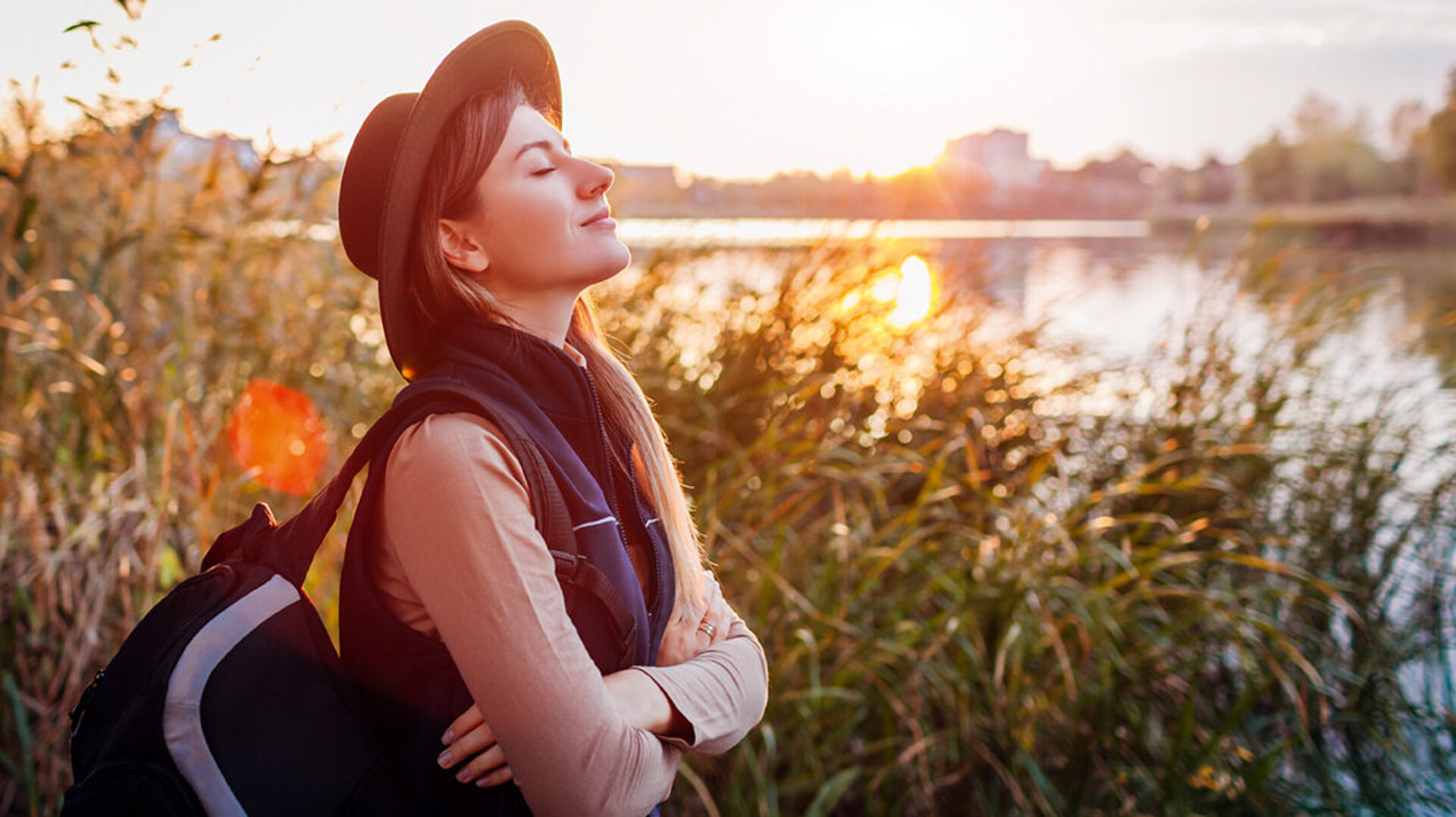 © Maryviolet - AdobeStock.com Frau entspannt am Seeufer bei Sonnenuntergang und genießt die Natur
