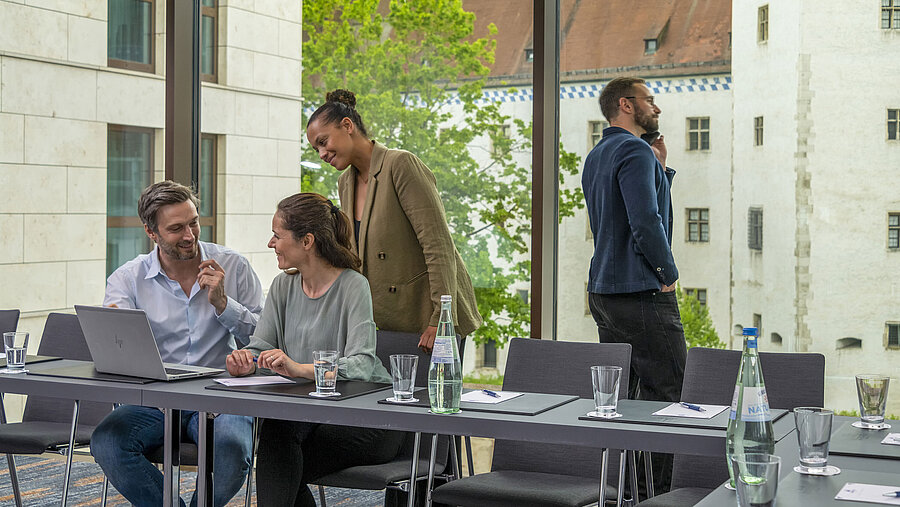 Lächelnde Geschäftsleute im Tagungsraum des Maritim Hotel Ingolstadt mit Blick auf historische Gebäude.