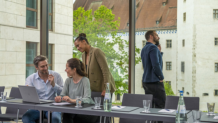 Lächelnde Geschäftsleute im Tagungsraum des Maritim Hotel Ingolstadt mit Blick auf historische Gebäude.