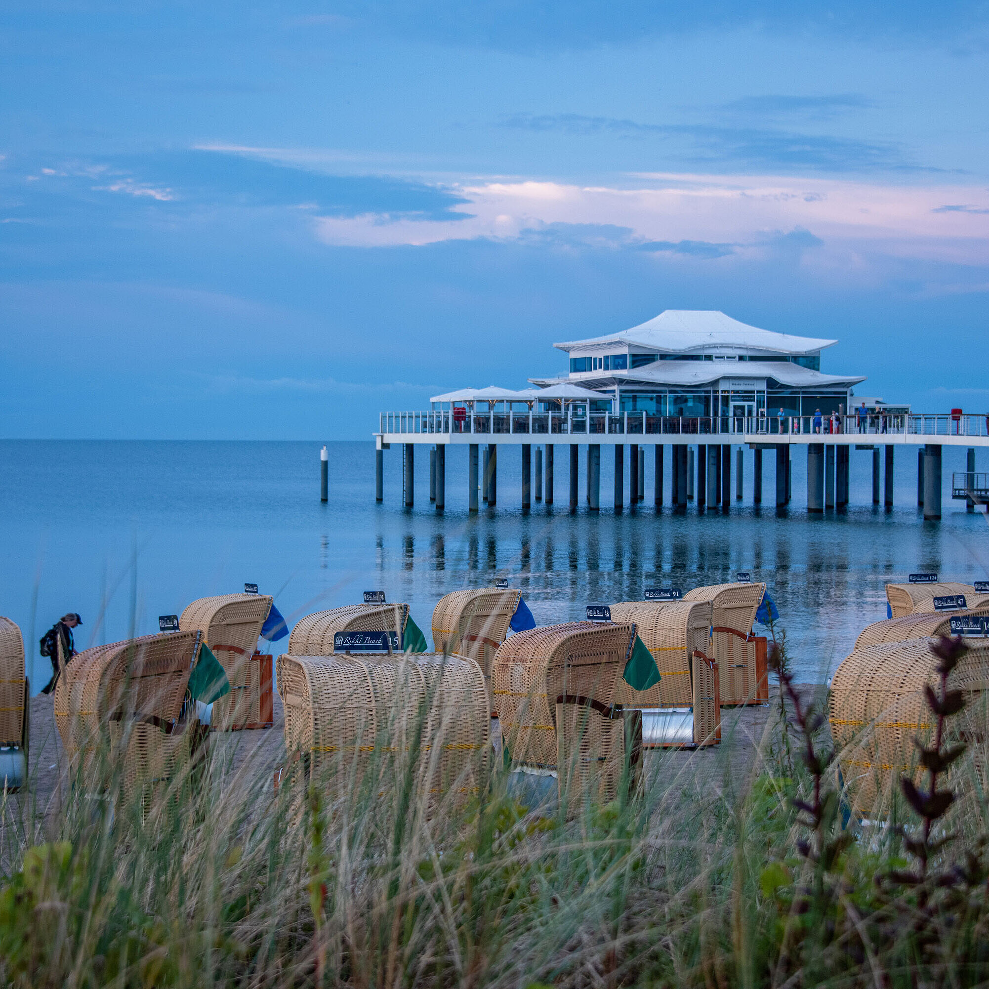 Strandkörbe und Seebrücke bei Sonnenuntergang Strandkörbe am Sandstrand mit Blick auf die Ostsee und eine Seebrücke bei Sonnenuntergang.