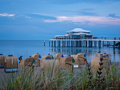 Strandkörbe und Seebrücke bei Sonnenuntergang Strandkörbe am Sandstrand mit Blick auf die Ostsee und eine Seebrücke bei Sonnenuntergang.