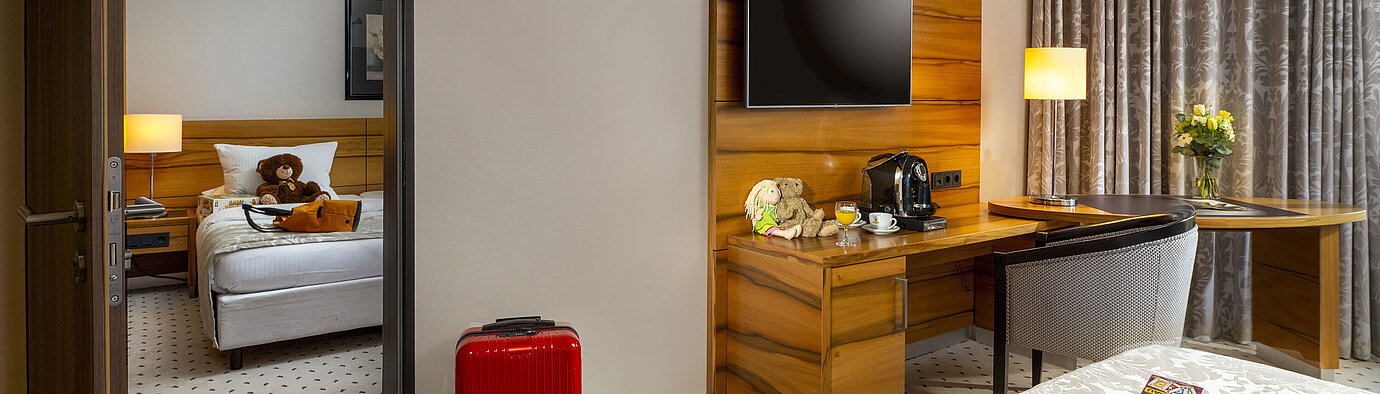 Familienzimmer im Maritim Hotel Bad Homburg mit getrenntem Kinderzimmer, Kuscheltieren und roten Koffer.