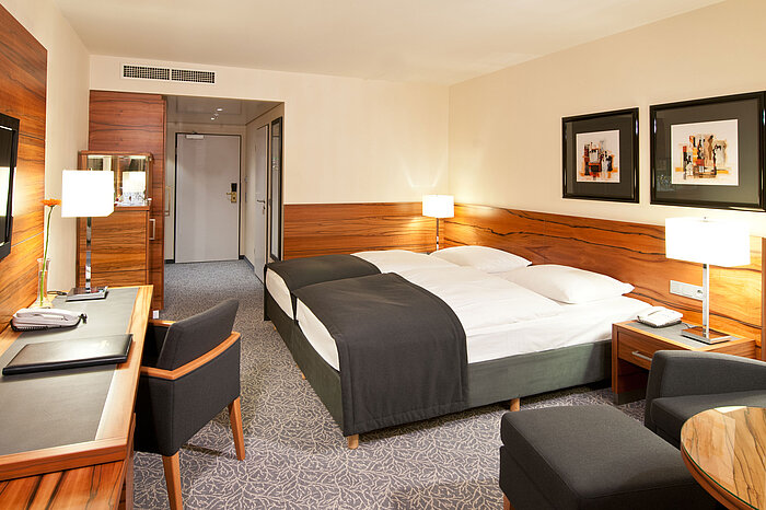 Doppelzimmer mit Holzdetails, Sitzgruppe und Schreibtisch im Maritim Hotel München