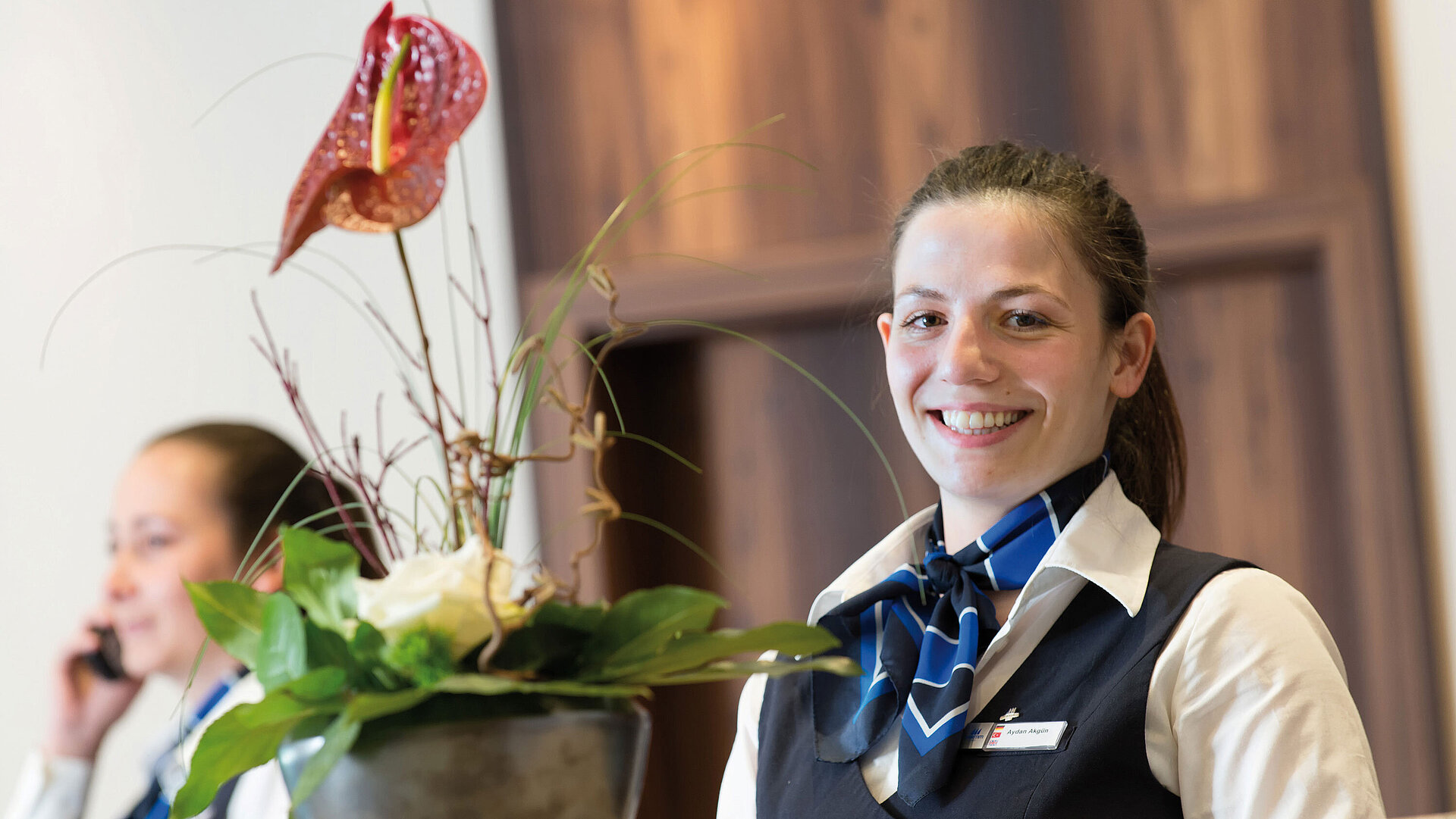 Freundliche Mitarbeiterin an der Rezeption im Maritim Hotel Titisee mit Blumenschmuck im Vordergrund