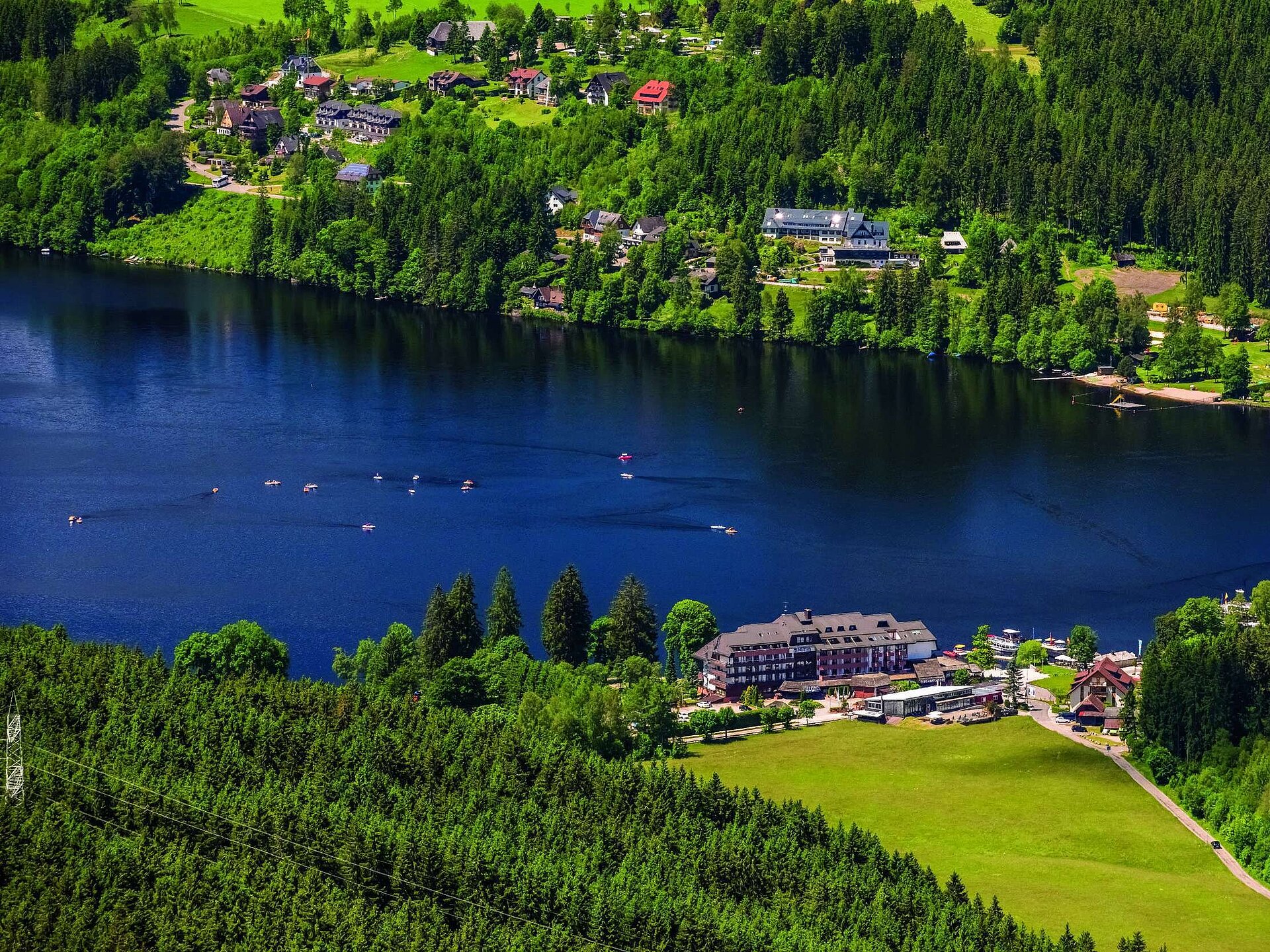 Vogelperspektive Luftaufnahme des Maritim Hotels direkt am Ufer des Titisees mit umliegendem Wald und Tretbooten auf dem Wasser