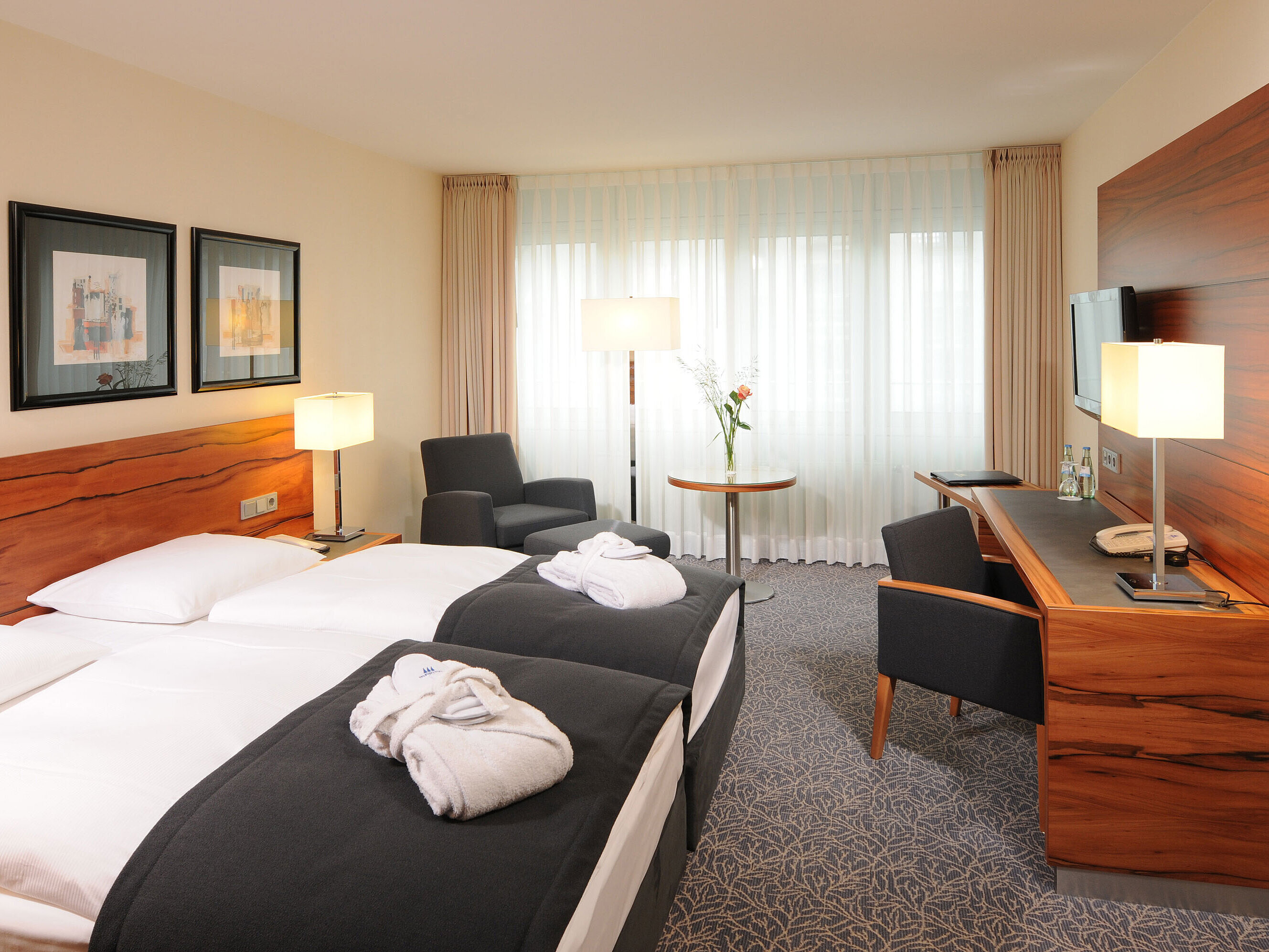 Helles Doppelzimmer mit Schreibtisch, Sesseln und Bademänteln im Maritim Hotel München