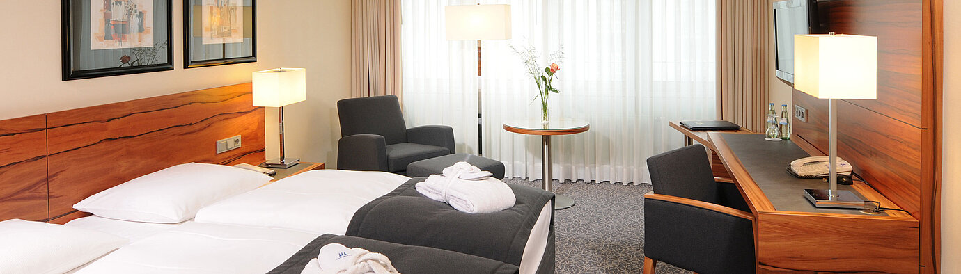 Helles Doppelzimmer mit Schreibtisch, Sesseln und Bademänteln im Maritim Hotel München
