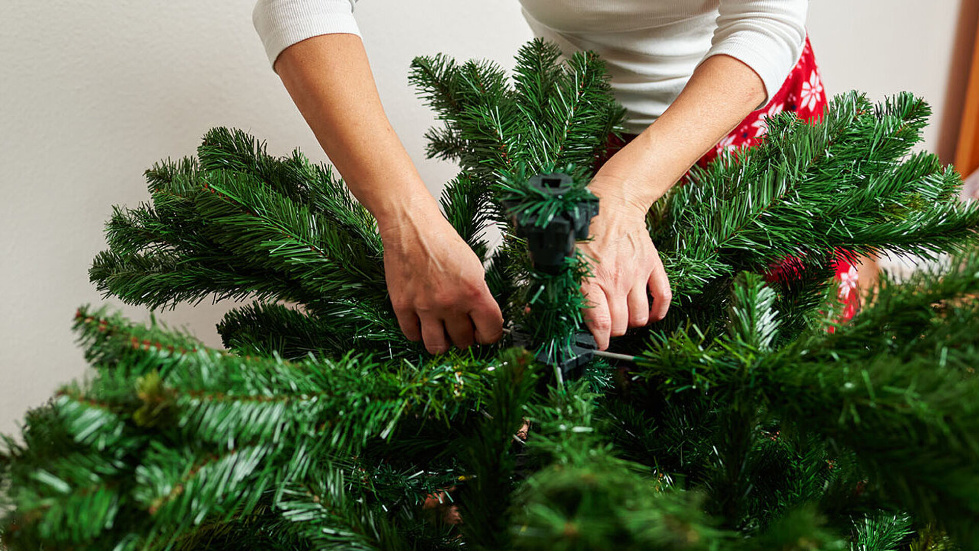 Hände richten Zweige eines künstlichen Weihnachtsbaums