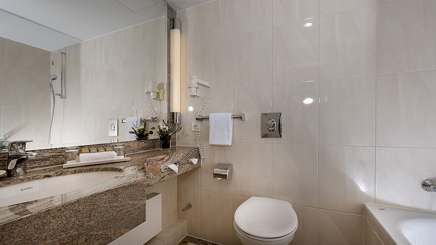 Modernes Badezimmer im Maritim Seehotel Timmendorfer Strand mit Waschtisch, Spiegel, Dusche, WC und Badewanne.