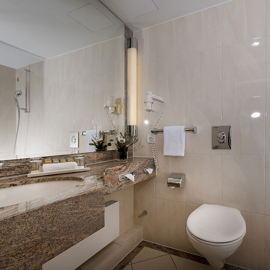 Modernes Badezimmer im Maritim Seehotel Timmendorfer Strand mit Waschtisch, Spiegel, Dusche, WC und Badewanne.