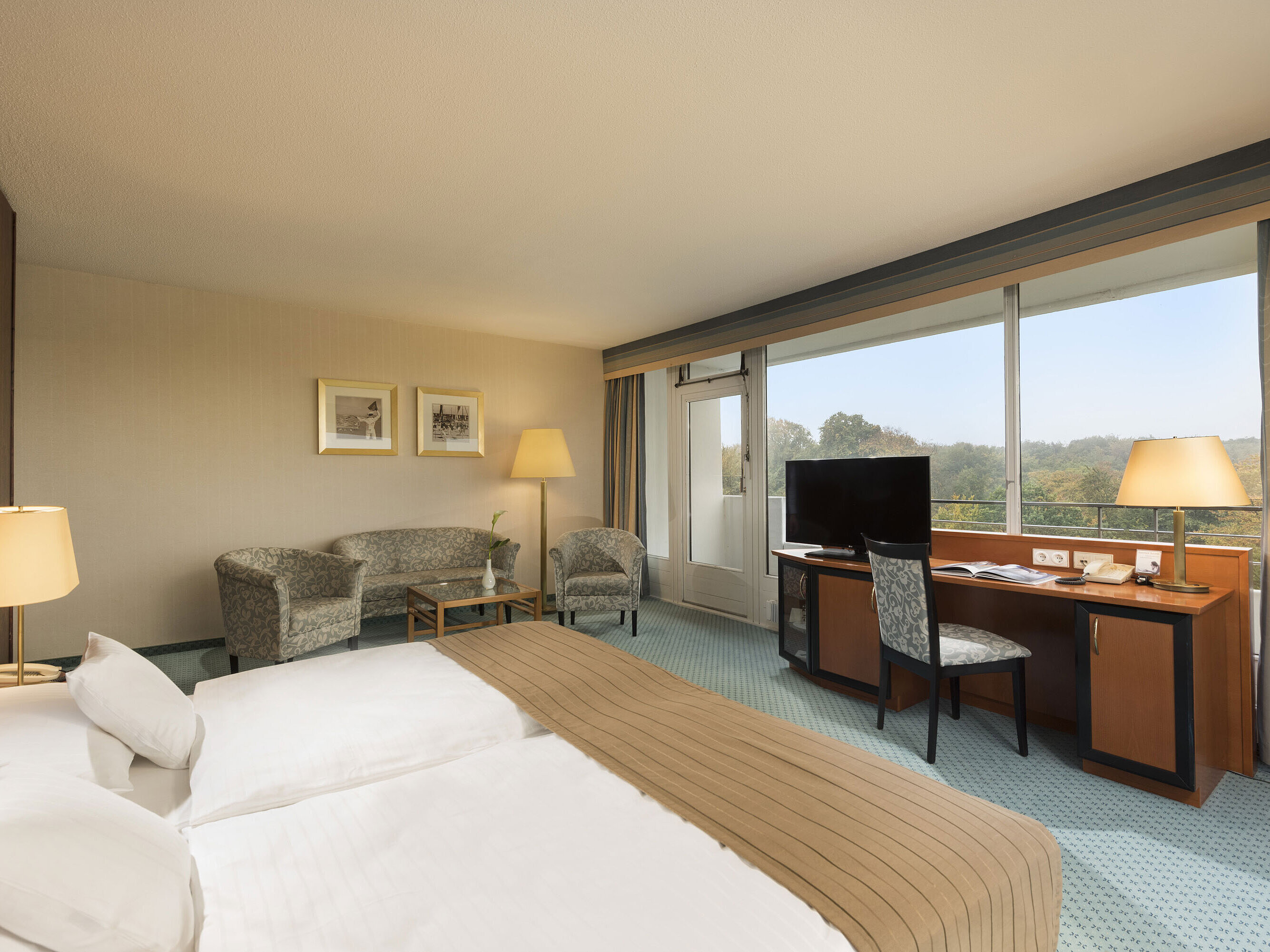 Comfort Zimmer im Maritim Hotel Kiel mit gemütlicher Sitzecke, Schreibtisch, großem Bett und herrlichem Blick ins Grüne.
