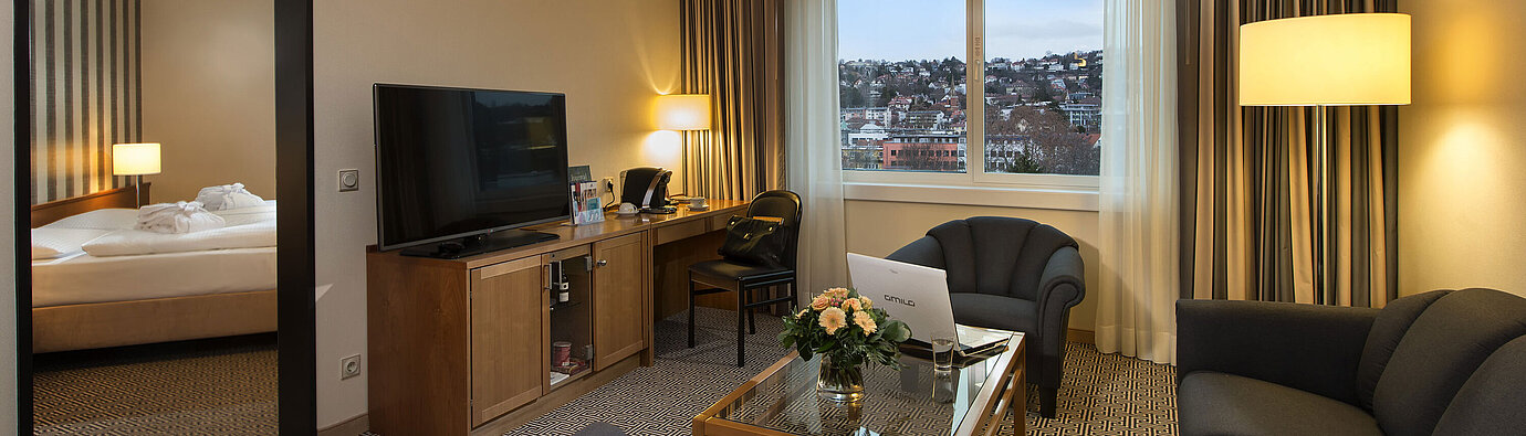 Junior Suite Wohnbereich der Suite mit Sofa, TV, Schreibtisch und Blick auf die Stadt im Maritim Hotel Stuttgart