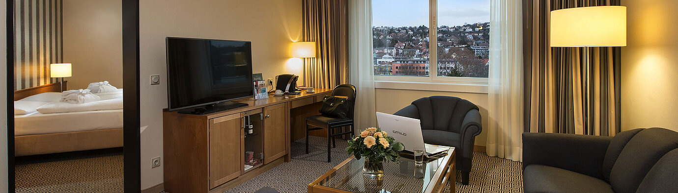 Wohnbereich der Suite mit Sofa, TV, Schreibtisch und Blick auf die Stadt im Maritim Hotel Stuttgart