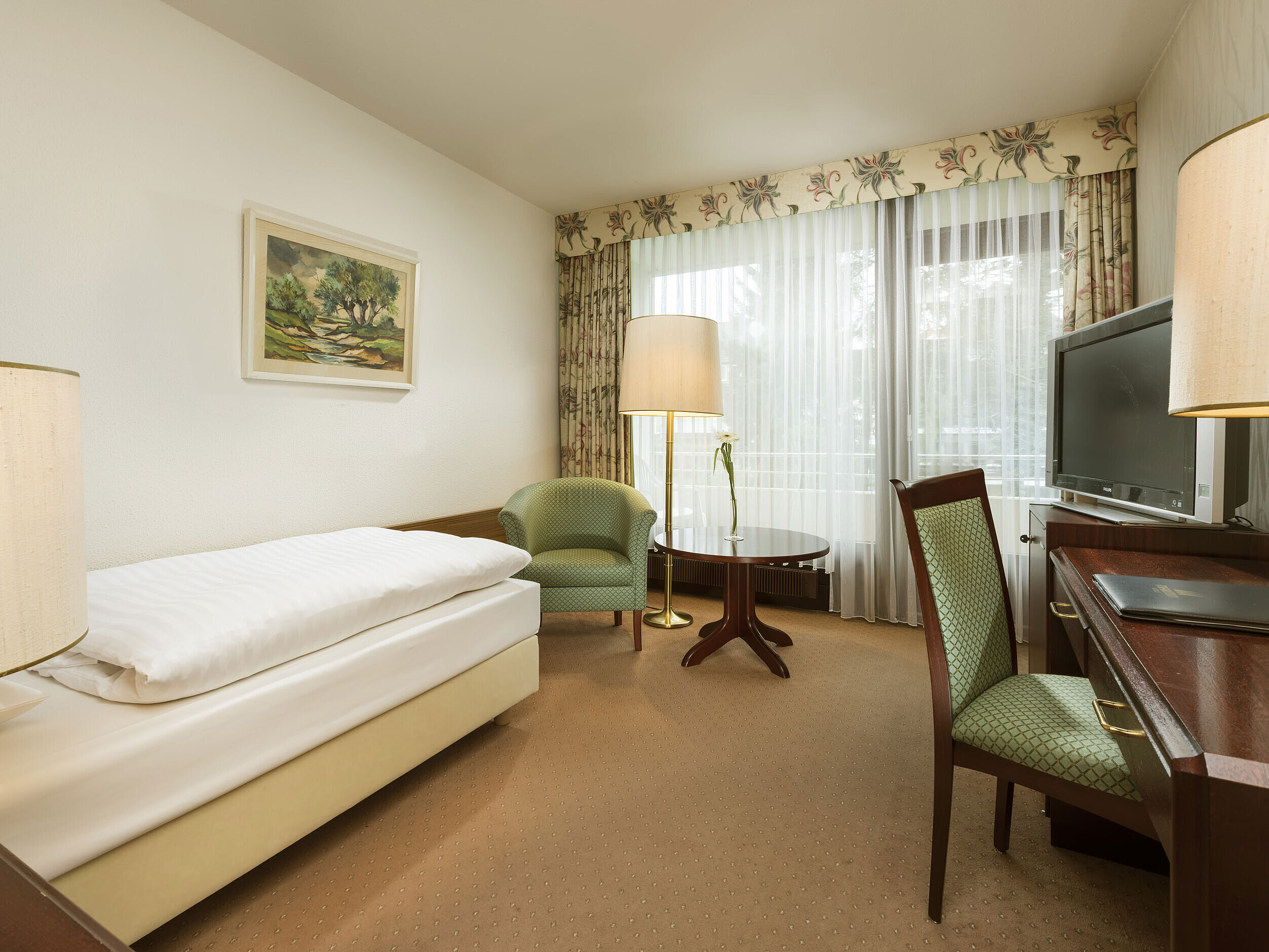 Einzelzimmer mit Schreibtisch, Sessel und Balkonzugang im Maritim Hotel Bad Salzuflen