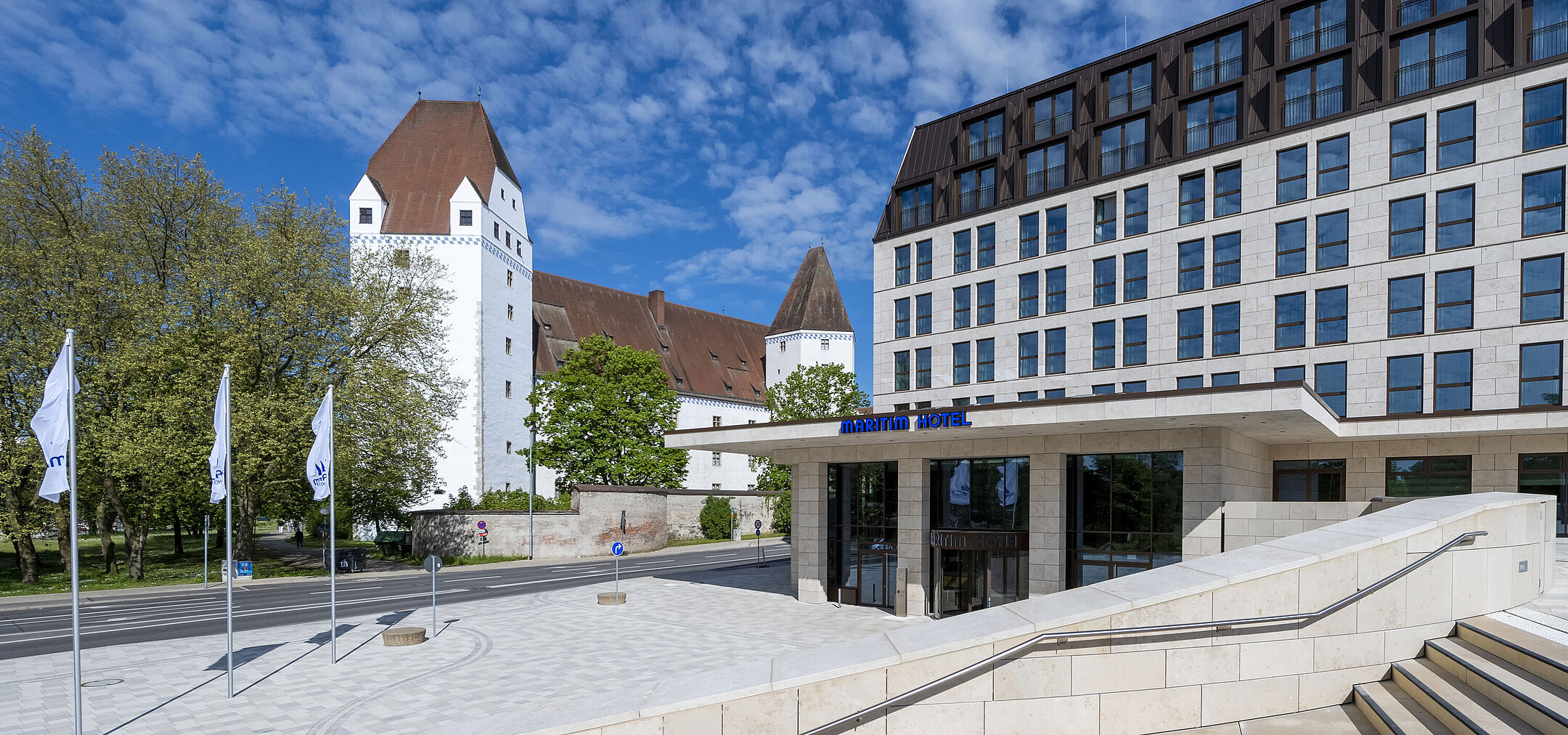 Modernes Maritim Hotel Ingolstadt mit dem historischen Neuen Schloss im Hintergrund und einladendem Eingangsbereich.