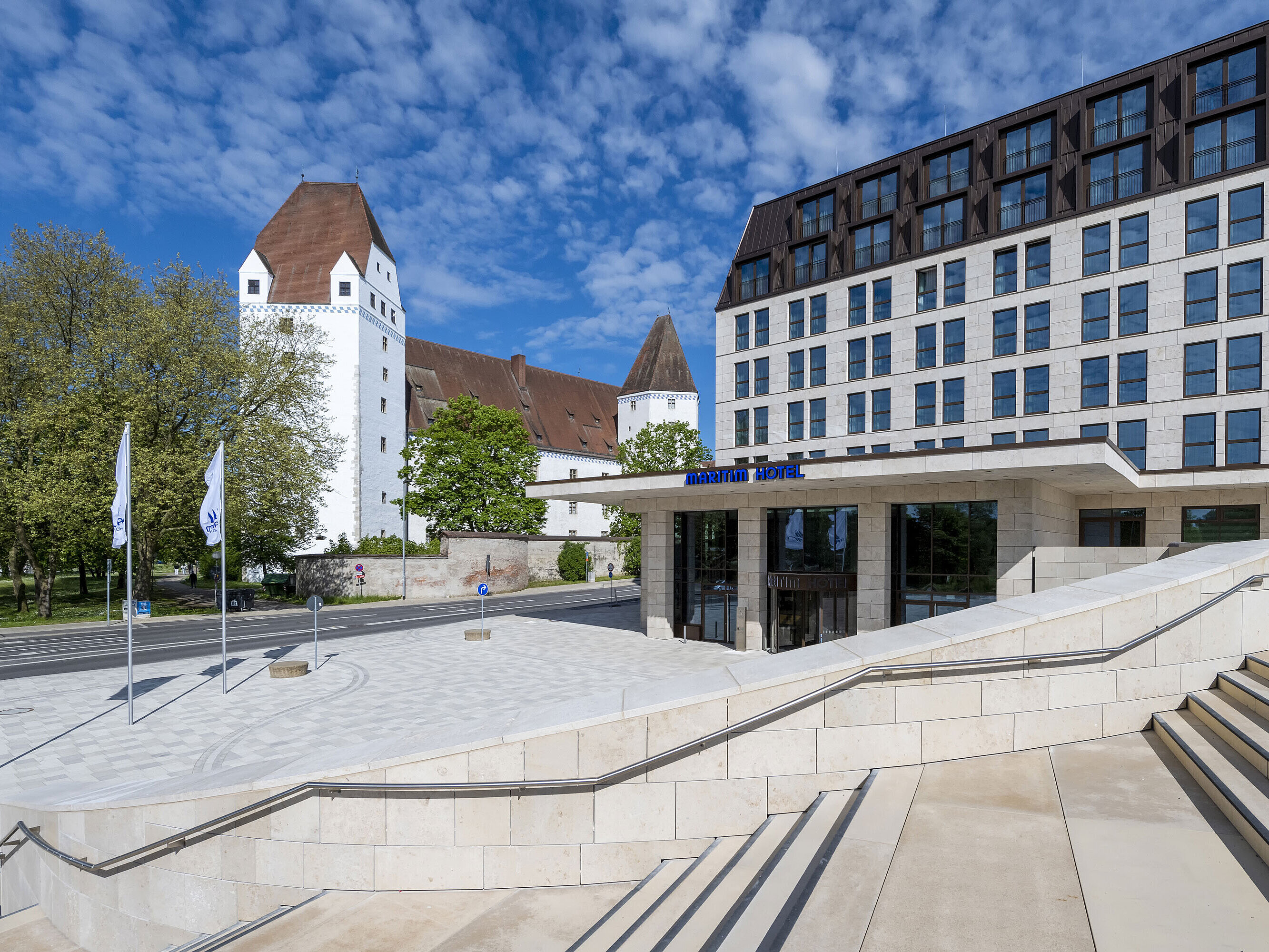 Das moderne Maritim Hotel Ingolstadt mit dem historischen Neuen Schloss im Hintergrund und einladendem Eingangsbereich.