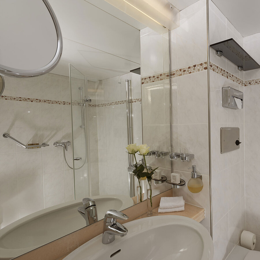 Helles Bad im Maritim Hotel Bad Salzuflen mit Dusche, großem Spiegel und weißen Fliesen