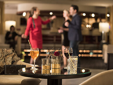 Tisch mit Cocktails und Drinks, während Gäste in der Bar des Maritim Seehotel Timmendorfer Strand tanzen.