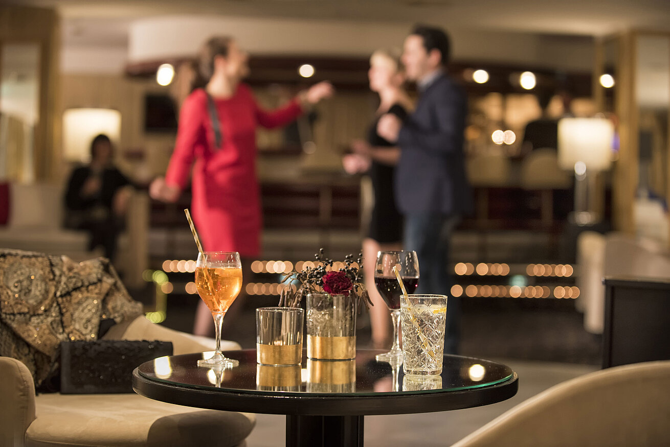 Tisch mit Cocktails und Drinks, während Gäste in der Bar des Maritim Seehotel Timmendorfer Strand tanzen.
