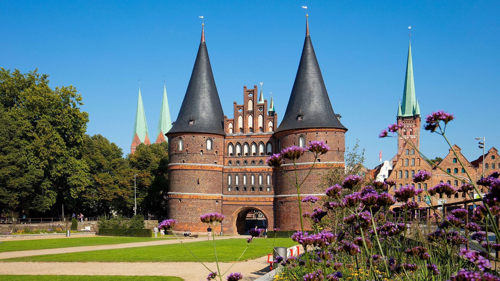 Holstentor Lübeck Holstentor in Lübeck mit blühenden Blumen im Vordergrund und blauem Himmel.