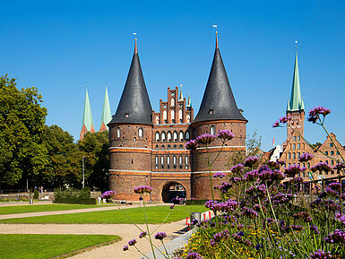 Holstentor Lübeck Holstentor in Lübeck mit blühenden Blumen im Vordergrund und blauem Himmel.
