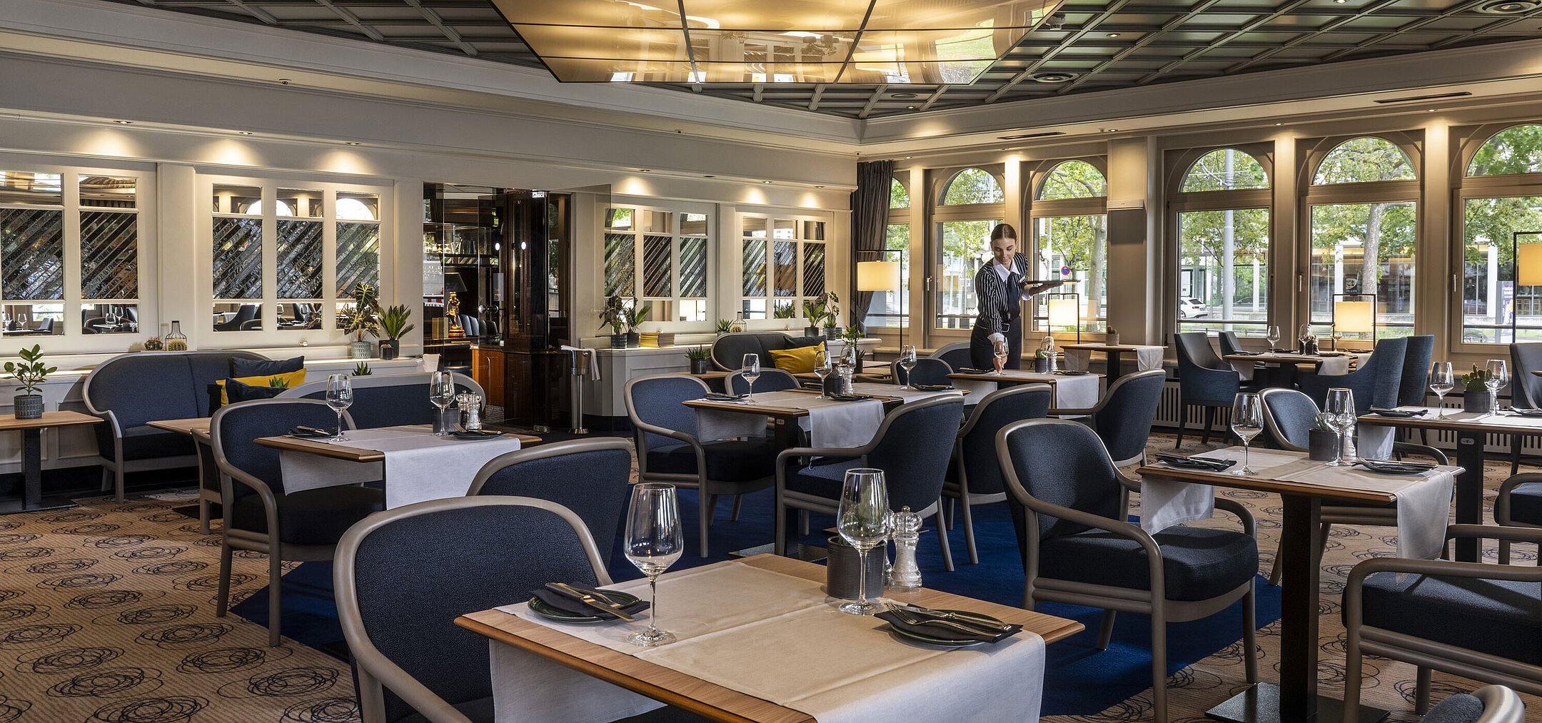 Modernes Restaurant im Maritim Darmstadt mit gedeckten Tischen und elegantem Design. Eine Mitarbeiterin sorgt für den Service