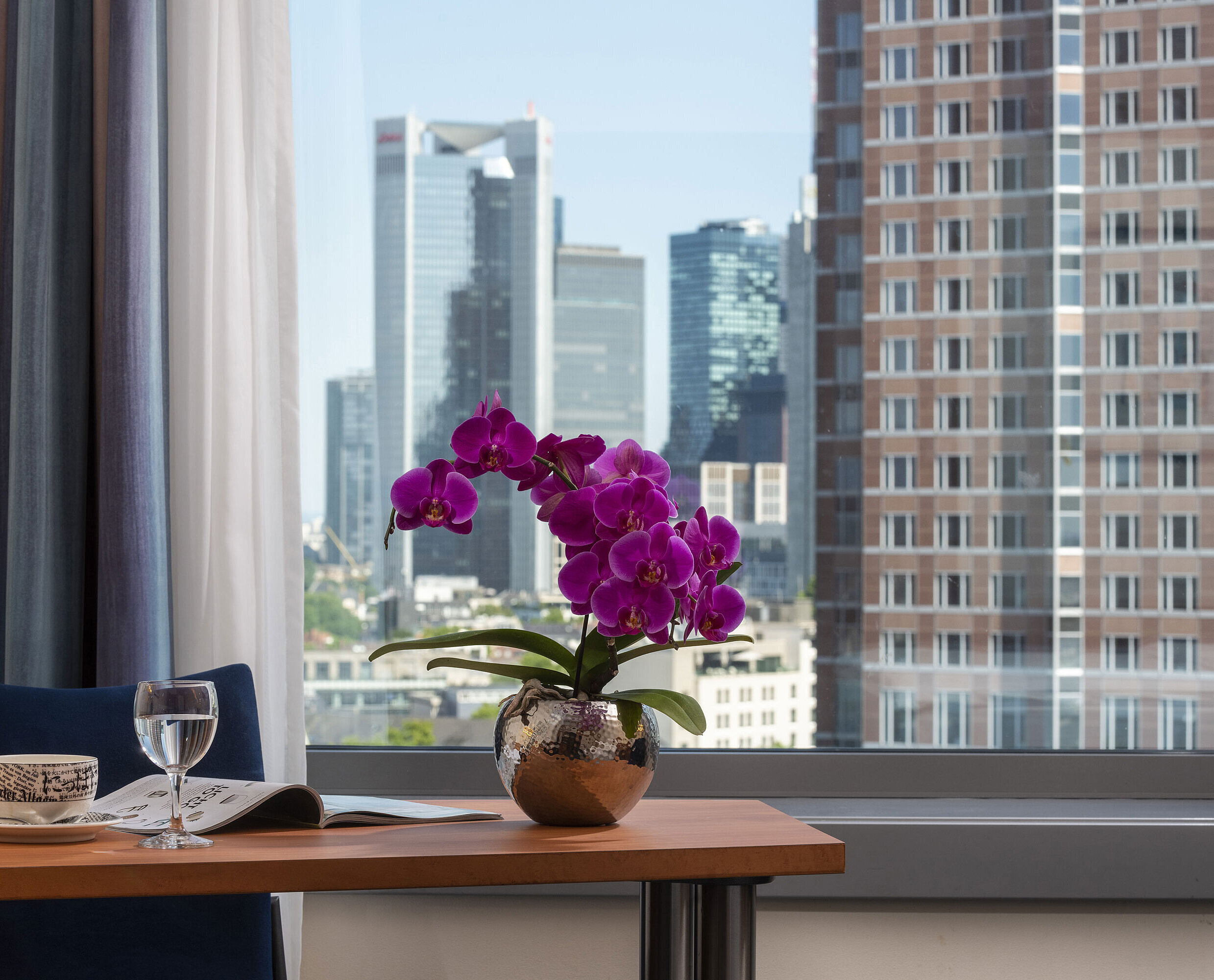 Ausblick aus dem Zimmer im Maritim Hotel Frankfurt mit Skyline-Panorama, Schreibtisch und eleganter Orchidee.