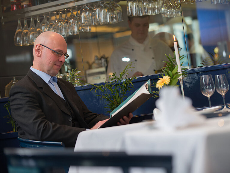 Restaurant Eleganter gedeckter Tisch im Restaurant des Maritim Hotel Magdeburg mit einem Gast beim Studieren der Speisekarte.