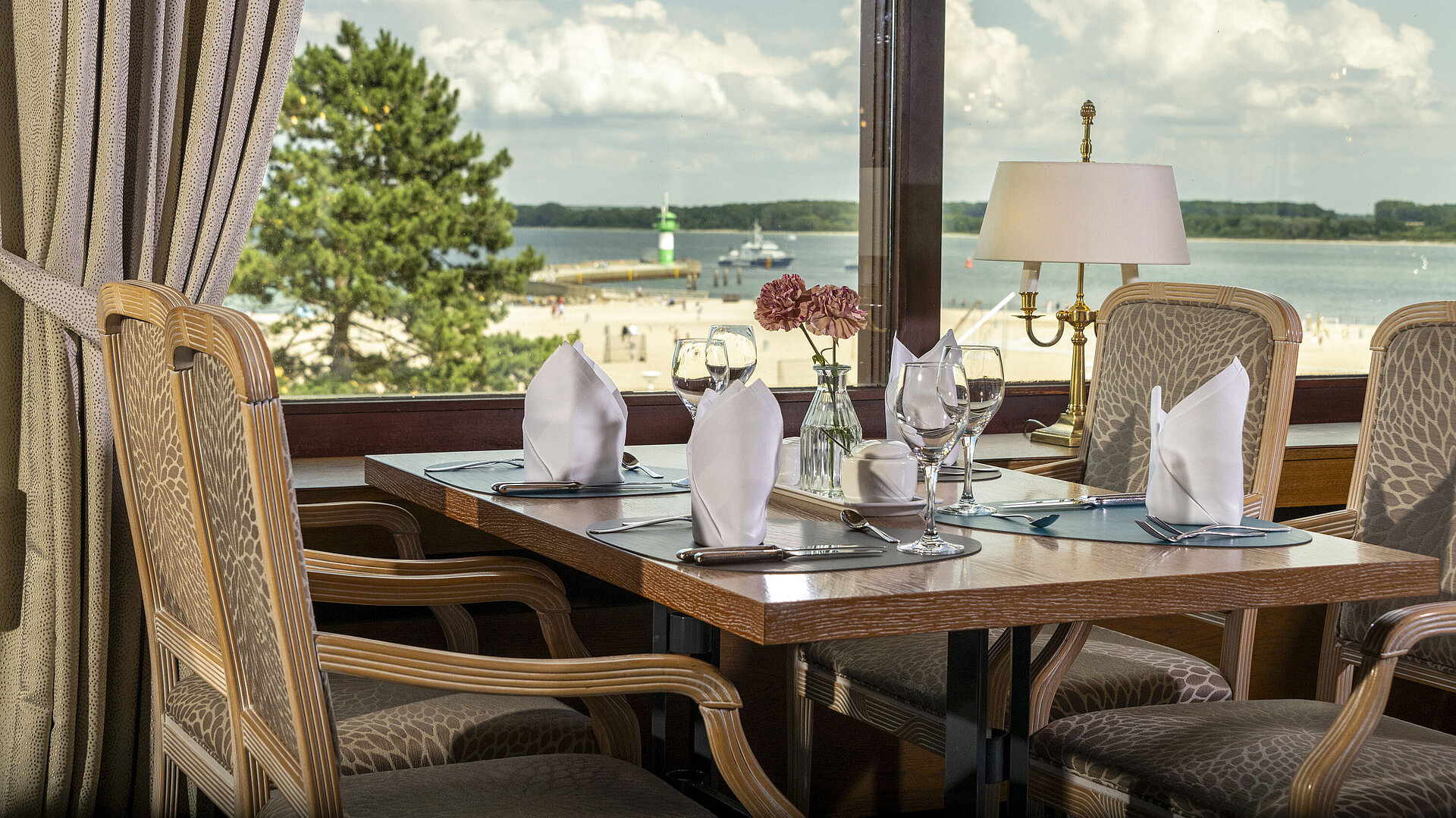 Ostseerestaurant Gedeckter Tisch am Fenster mit Ausblick auf den Strand und Leuchtturm im Maritim Hotel Travemünde