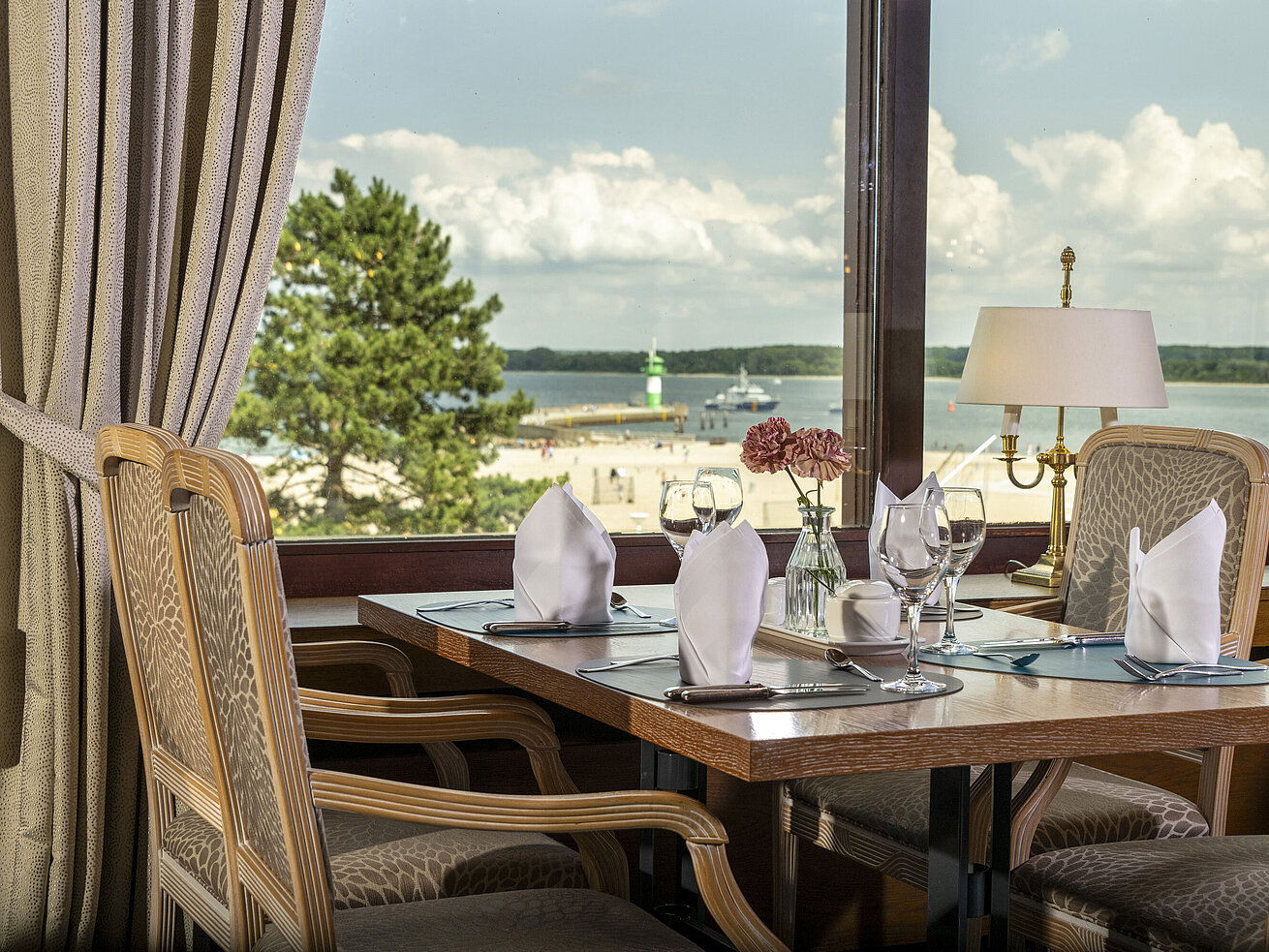 Gedeckter Tisch am Fenster mit Ausblick auf den Strand und Leuchtturm im Maritim Hotel Travemünde