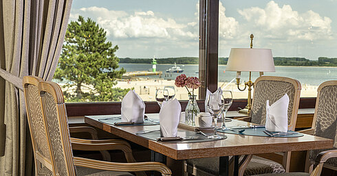 Gedeckter Tisch am Fenster mit Ausblick auf den Strand und Leuchtturm im Maritim Hotel Travemünde