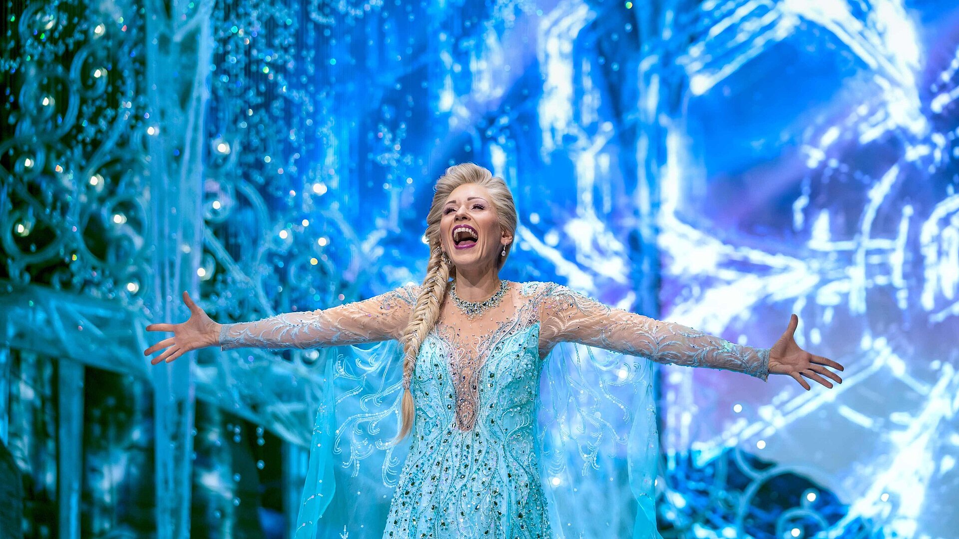 Darstellerin als Eiskönigin in funkelndem blauen Kostüm auf eisiger Bühnenkulisse