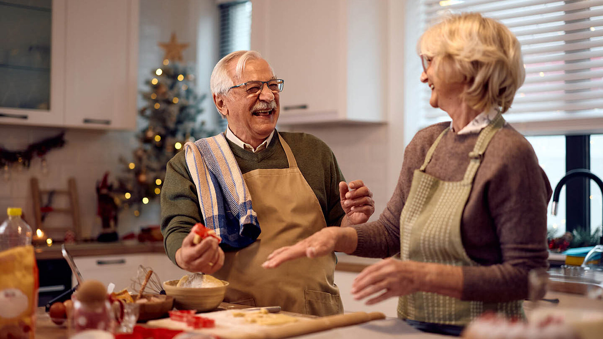 Älteres Paar backt gemeinsam in einer weihnachtlich dekorierten Küche und lacht miteinander.