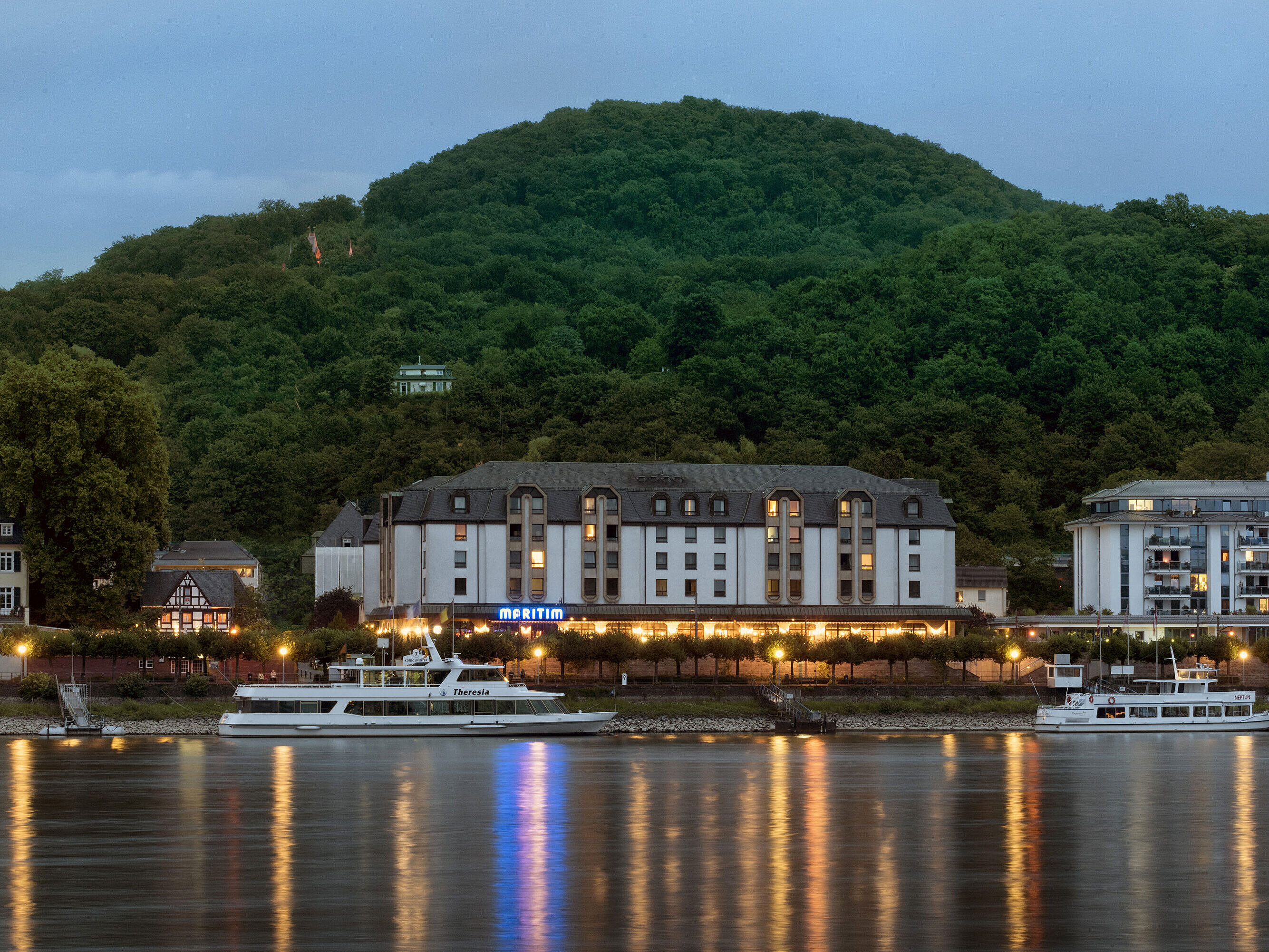 Das Maritim Hotel Königswinter bei Nacht mit stimmungsvoller Beleuchtung und Blick auf den Rhein.