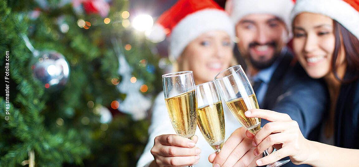 © pressmaster - fotolia Freunde mit Weihnachtsmützen stoßen mit Sektgläsern vor festlich geschmücktem Weihnachtsbaum a