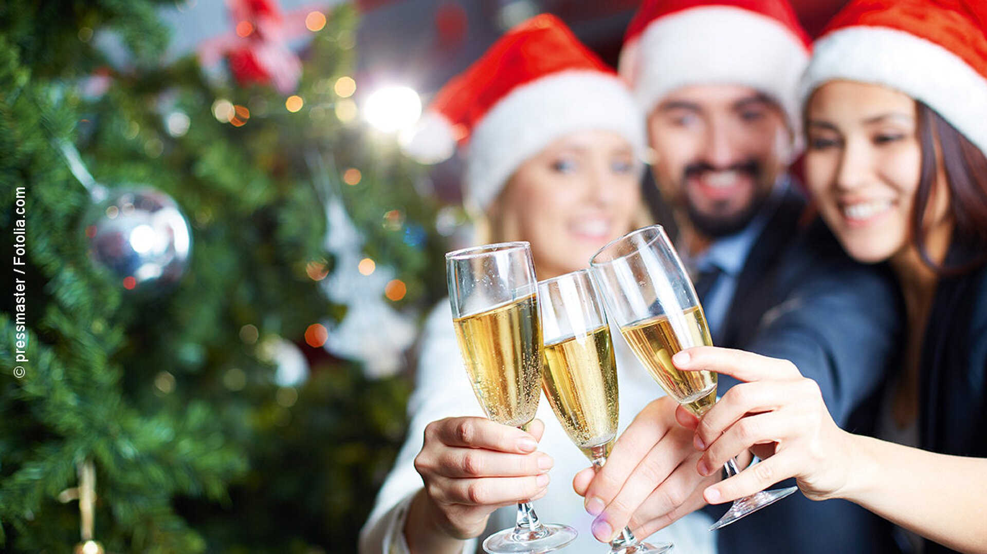 © pressmaster - fotolia Freunde mit Weihnachtsmützen stoßen mit Sektgläsern vor festlich geschmücktem Weihnachtsbaum a