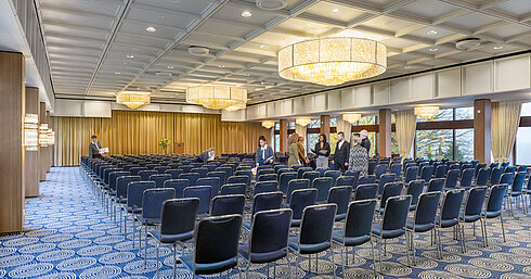 Saal Maritim im Maritim Hotel Kiel, großer Konferenzraum mit Reihenbestuhlung, Kronleuchtern und Bühne, Personal bereitet den Raum vor.