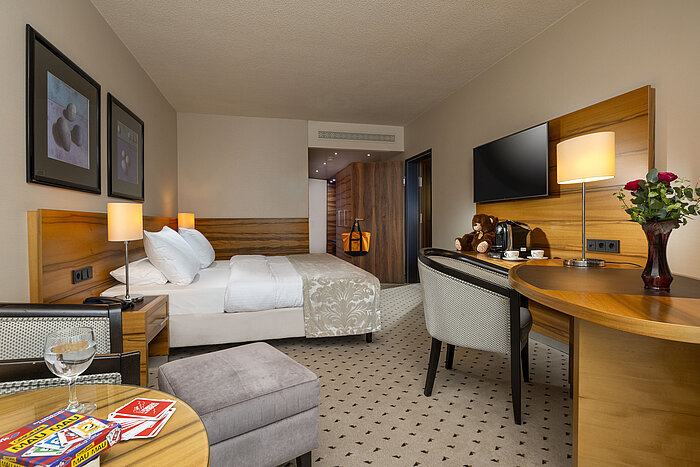 Komfortzimmer im Maritim Hotel Bad Homburg mit Doppelbett, Spielkarten, Kuscheltier und stilvollem Holzdekor.