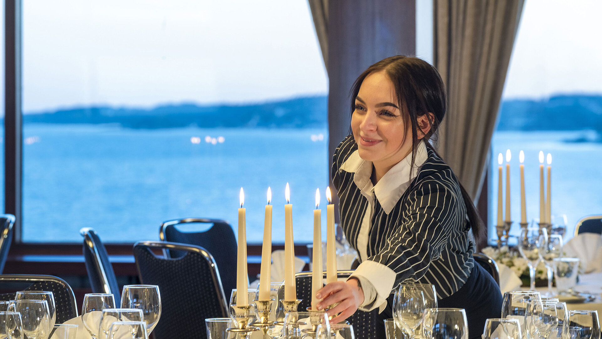 Saal Maritim im Maritim Hotel Kiel, eine Mitarbeiterin zündet Kerzen auf einem festlich gedeckten Tisch an, im Hintergrund Meerblick.