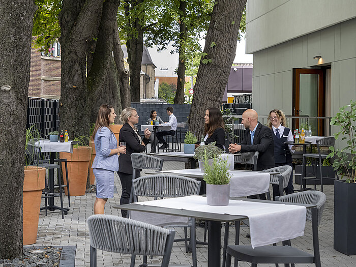 Moderne Terrasse im Maritim Hotel Darmstadt mit Gästen, die entspannen, Bäumen im Hintergrund und stilvollen grauen Möbeln.