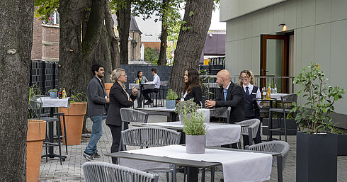Moderne Terrasse im Maritim Hotel Darmstadt mit Gästen, die entspannen, Bäumen im Hintergrund und stilvollen grauen Möbeln.