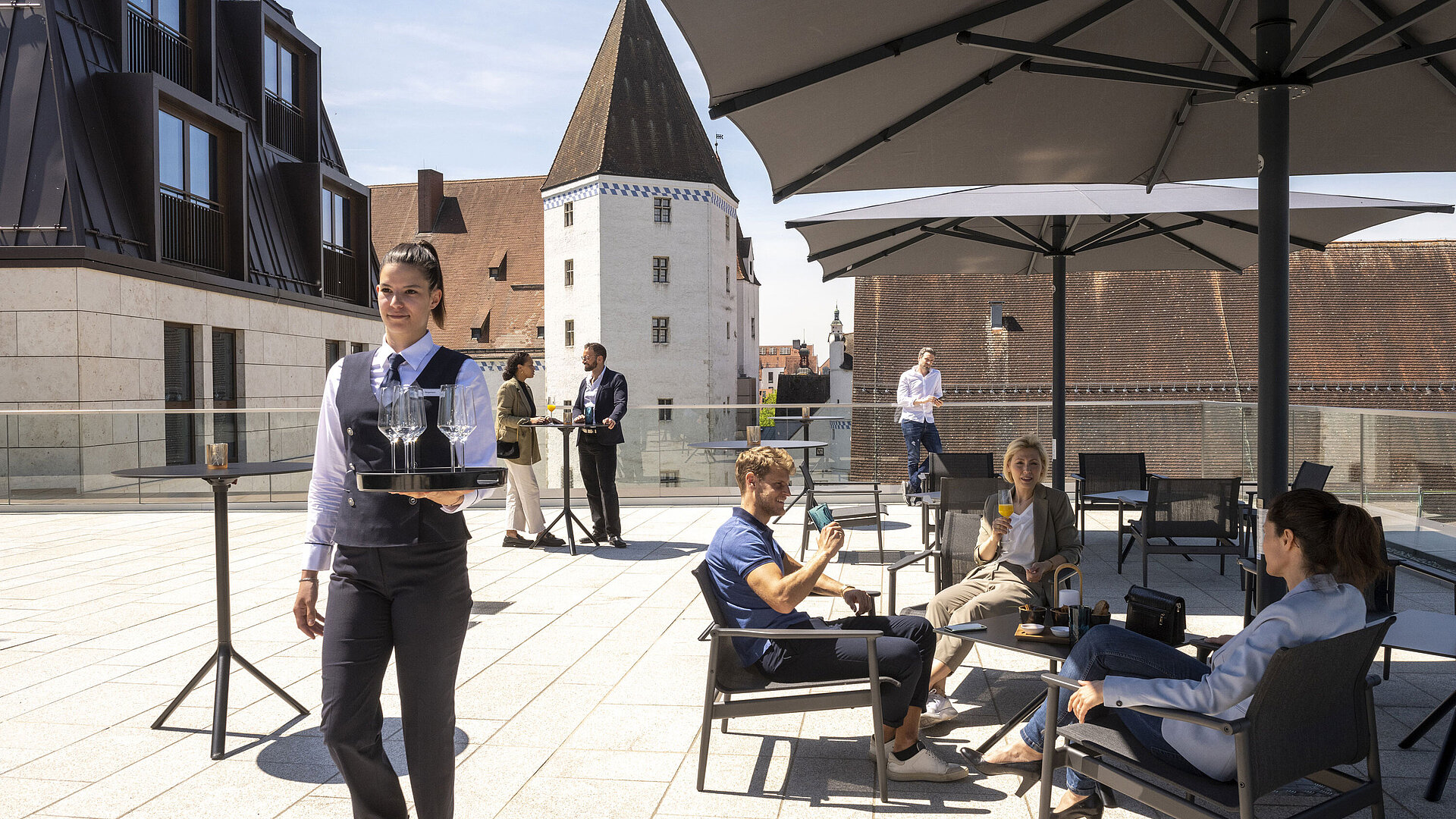 Gäste genießen Getränke auf der Dachterrasse des Maritim Hotel Ingolstadt mit Blick auf die Altstadt.