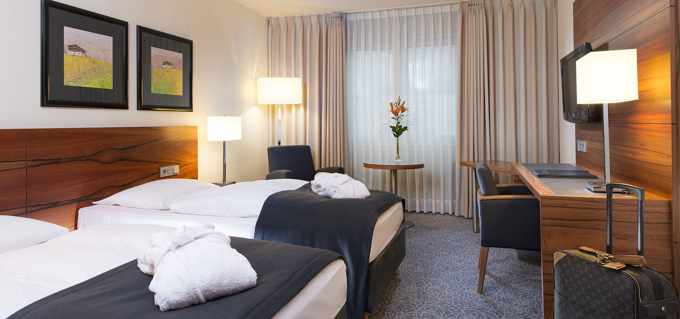 Komfortables Zweibettzimmer im Maritim Hotel München. Mit getrennten Betten, Schreibtisch, TV und Sitzbereich am Fenster. 