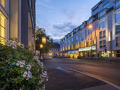 Abendliche Außenansicht des Maritim Hotel Würzburg mit beleuchteter Fassade und historischem Tor im Hintergrund