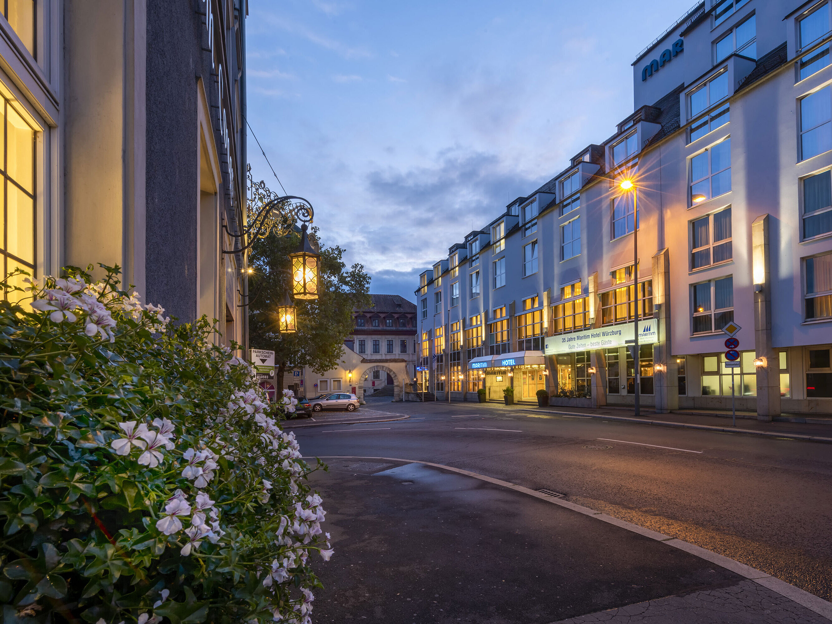 Abendliche Außenansicht des Maritim Hotel Würzburg mit beleuchteter Fassade und historischem Tor im Hintergrund