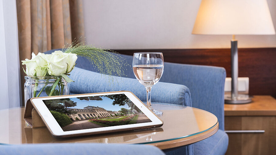 Gemütlicher Sitzbereich im Maritim Hotel Fulda mit Tablet, Glas Wasser und weißen Rosen auf einem Glastisch.