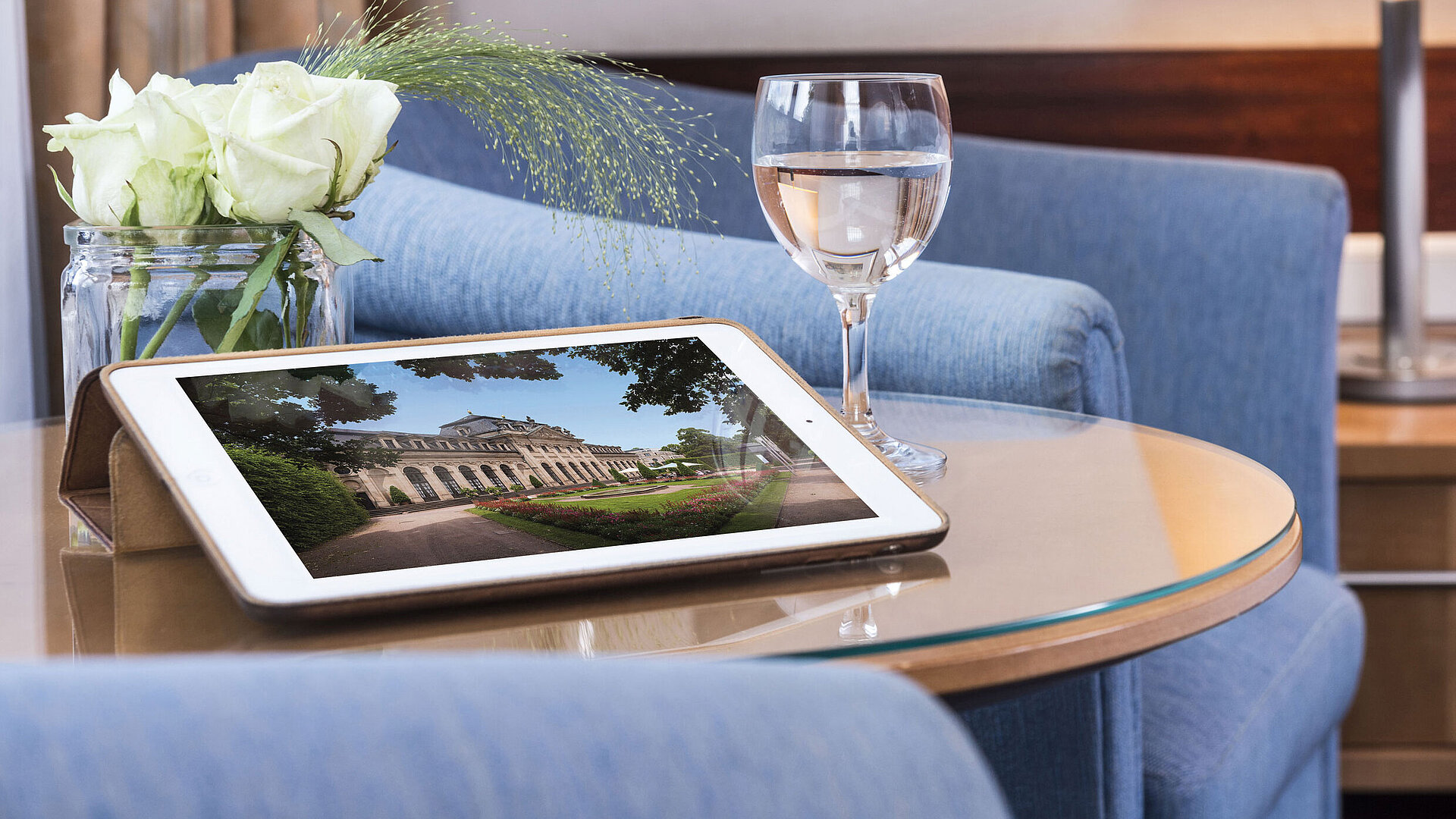 Gemütlicher Sitzbereich im Maritim Hotel Fulda mit Tablet, Glas Wasser und weißen Rosen auf einem Glastisch.