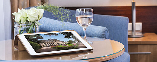 Gemütlicher Sitzbereich im Maritim Hotel Fulda mit Tablet, Glas Wasser und weißen Rosen auf einem Glastisch.