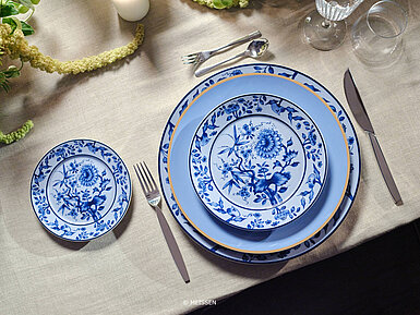Edles blaues Meissener Porzellan mit Blumenmuster auf festlich gedecktem Tisch mit Besteck und Gläsern